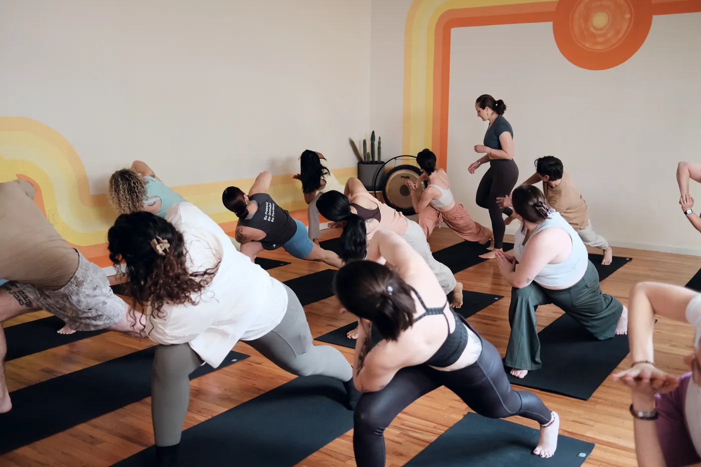 A full class moving through low lunges beneath the studio's sun mural