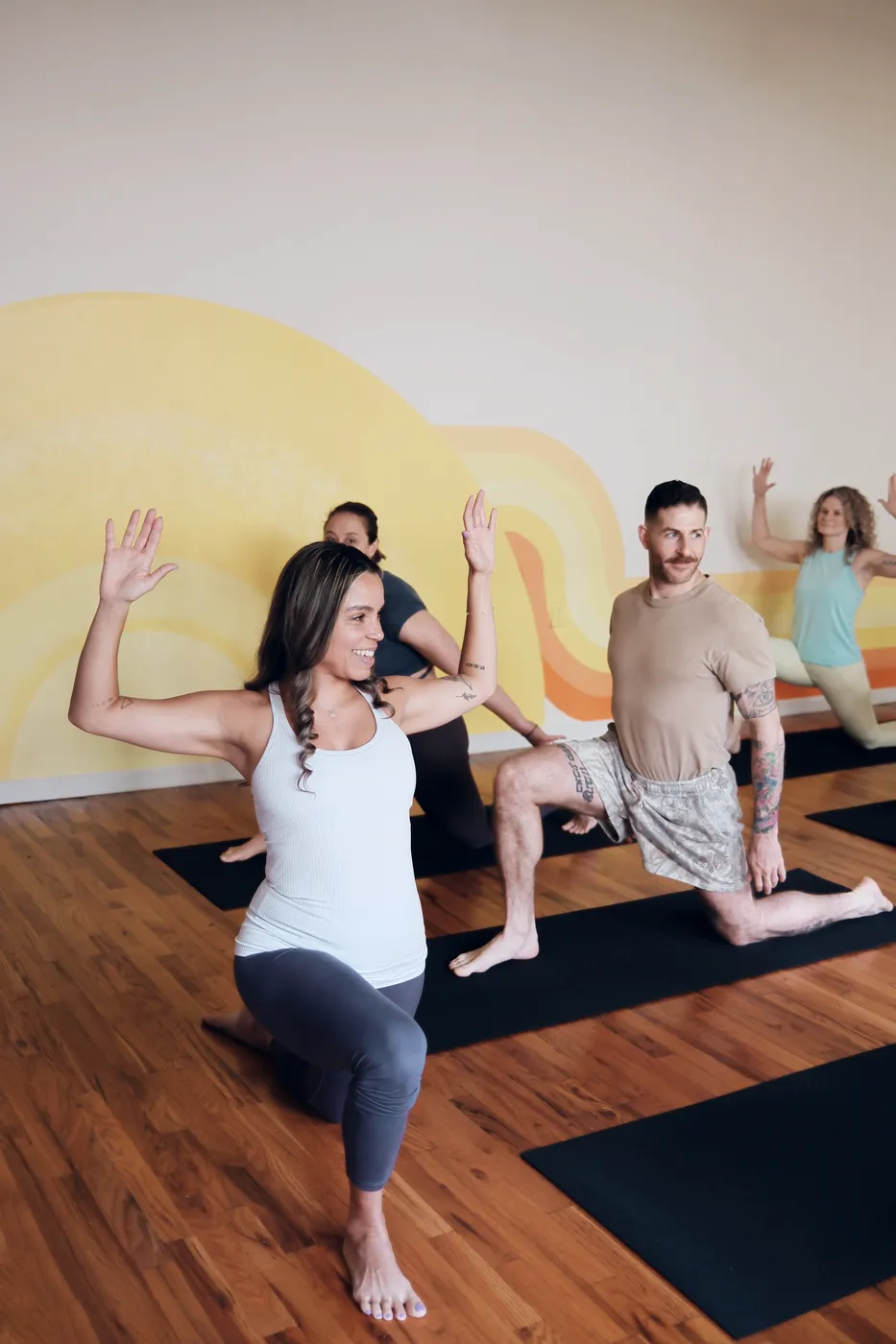 Students in low lunges with arms lifted in front of the yellow mural