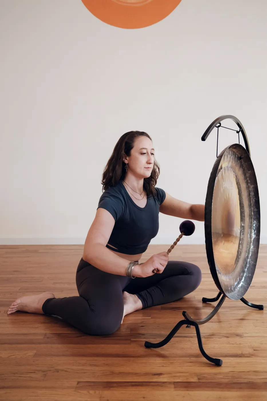 A teacher seated beside a gong, mallet in hand, ready for a sound bath