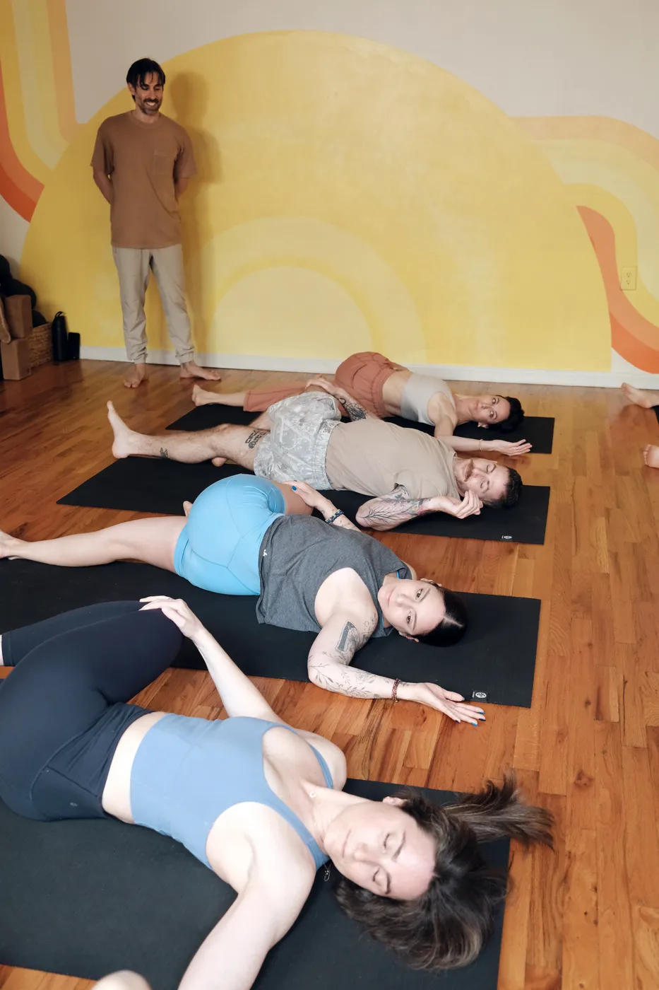 Students resting in reclined twists while the teacher looks on