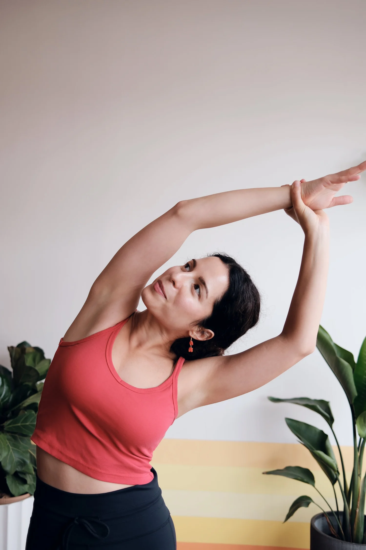 A student reaching overhead in a side stretch beside leafy plants